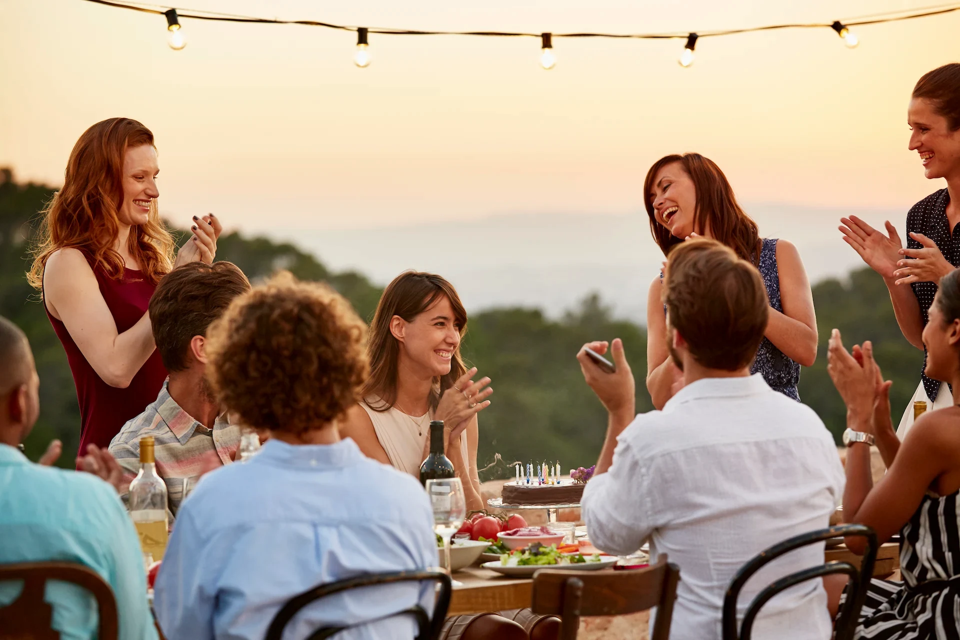 Group of friends joyfully celebrating a birthday outdoors with sea views at the Sanderling Hotel.