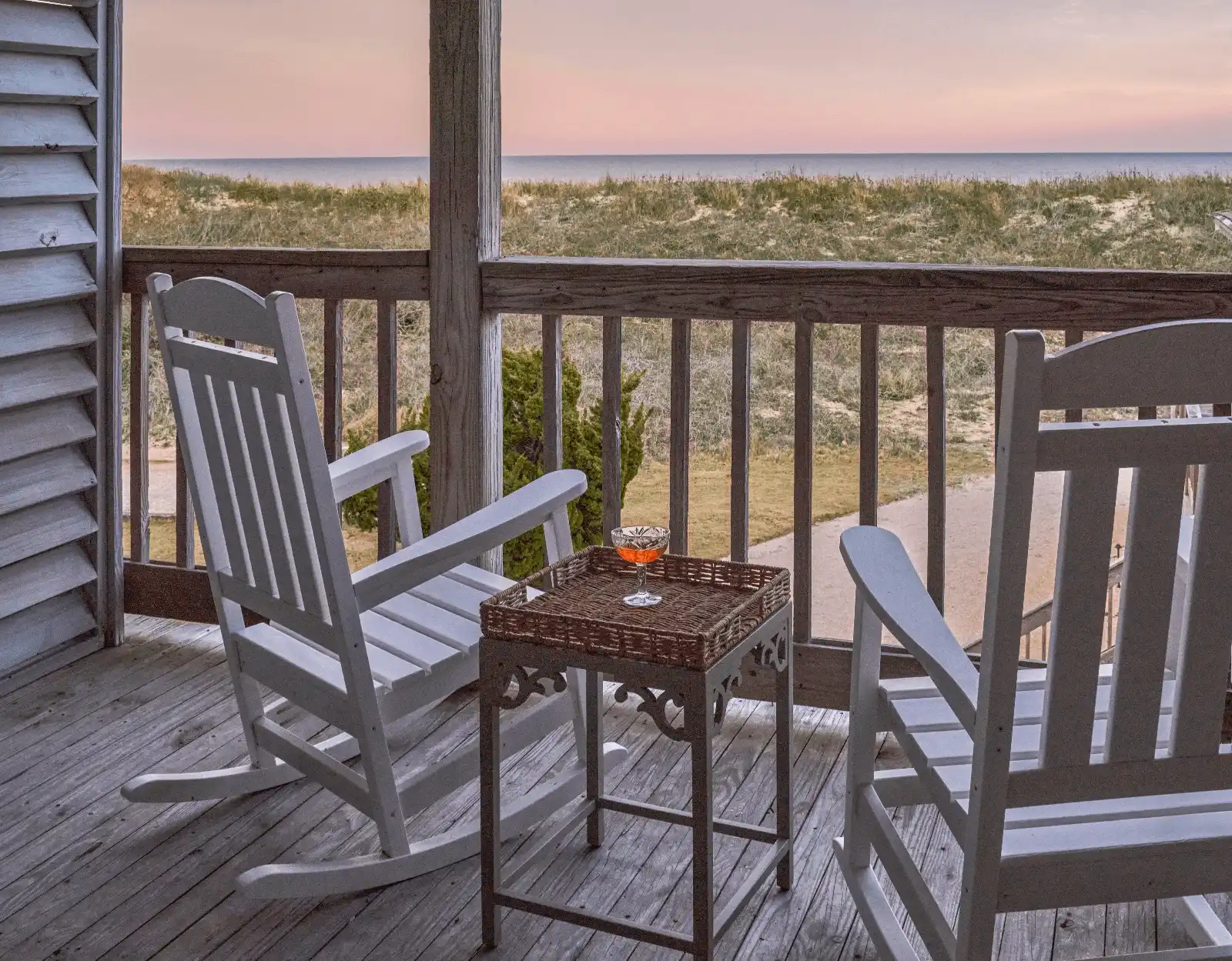 Terrace of the Sanderling Resort room, featuring two wooden chairs and a small table, overlooking the beach at sunset.