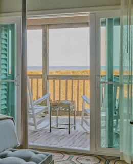 View from the room to the terrace, featuring two wooden chairs, a small table, and the serene sea in the background.