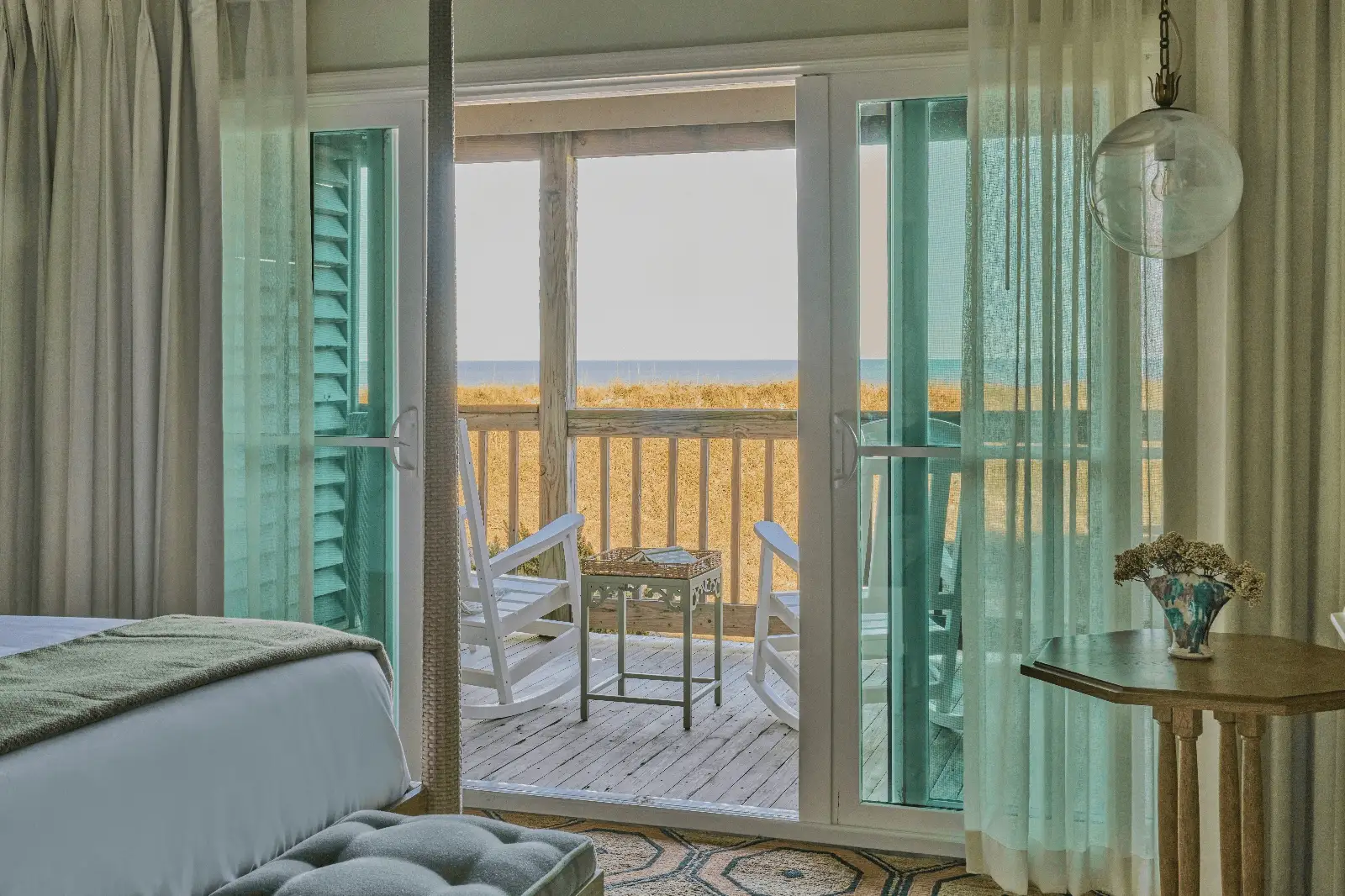 View from the room to the terrace, featuring two wooden chairs, a small table, and the serene sea in the background.