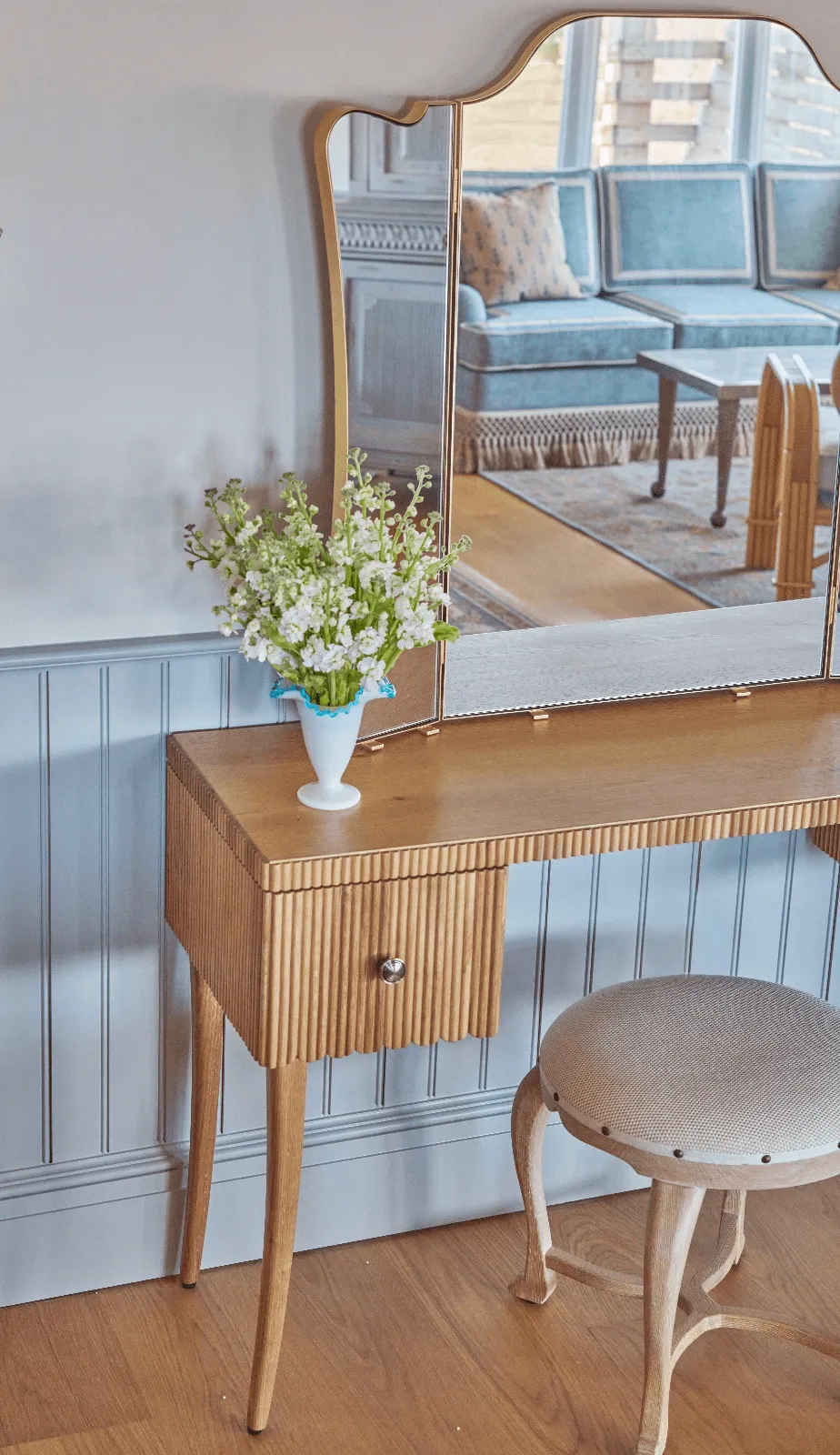 Elegant dresser with a mirror and fresh flowers, reflecting the cozy sofa of the Sanderling Hotel room in the background.