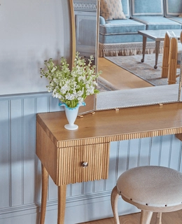 Elegant dresser with a mirror and fresh flowers, reflecting the cozy sofa of the Sanderling Hotel room in the background.